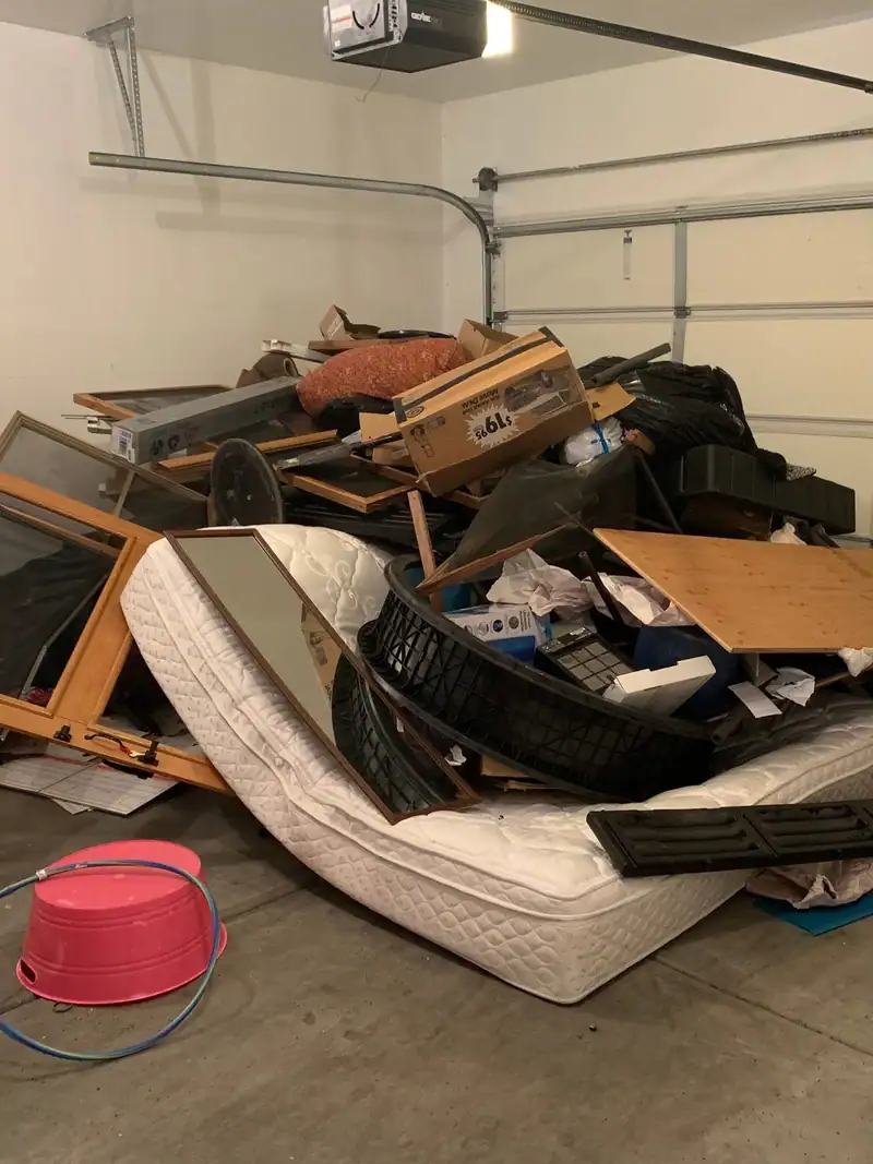 A garage piled with an old mattress, broken furniture and boxes
